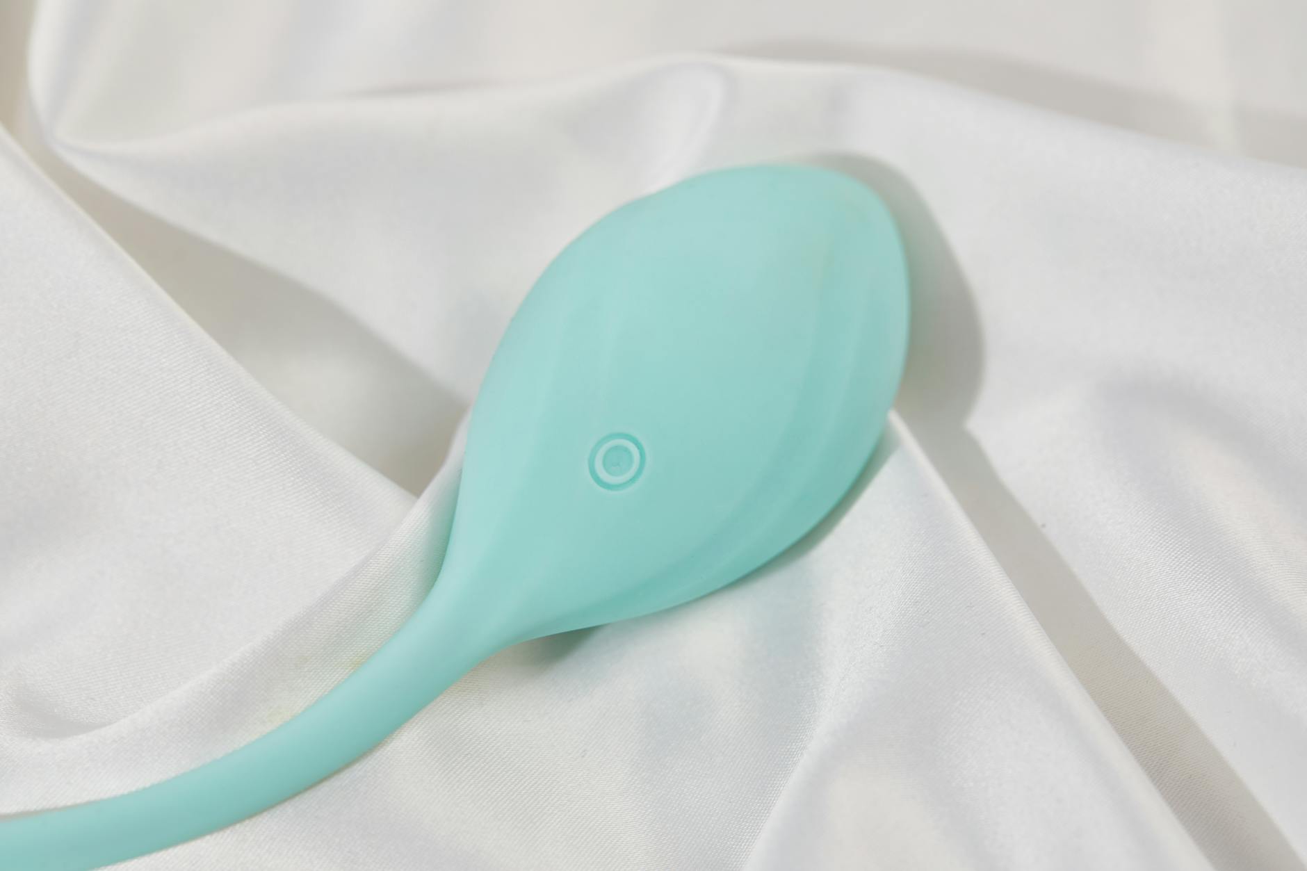 A teal lemon clitoral vibrator resting on white silk fabric, showcasing smooth design