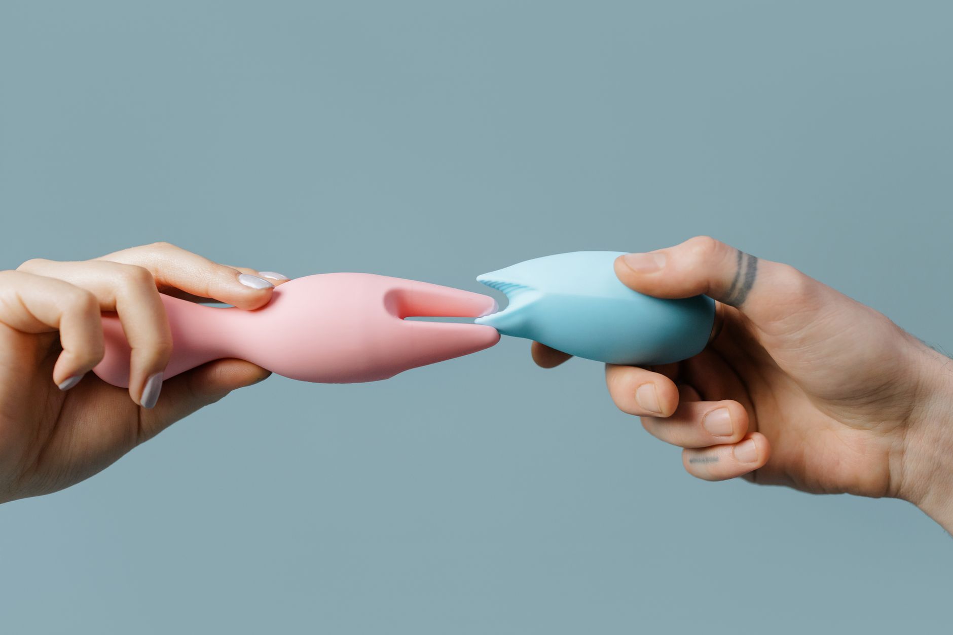 Colorful silicone clitoral vibrators held in hands on a neutral background