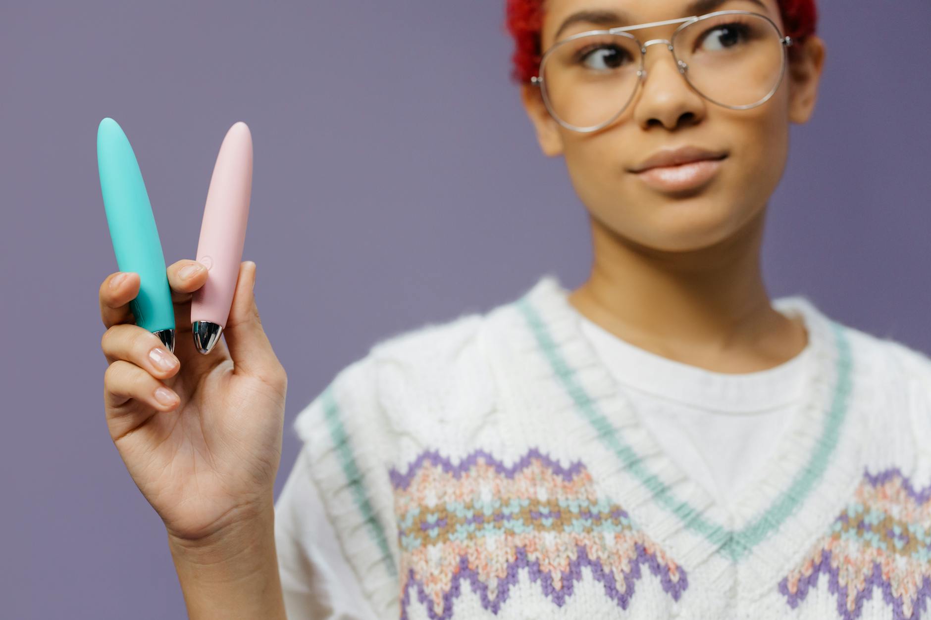 A woman holds colorful sex toys, including clitoral vibrators, against a purple background