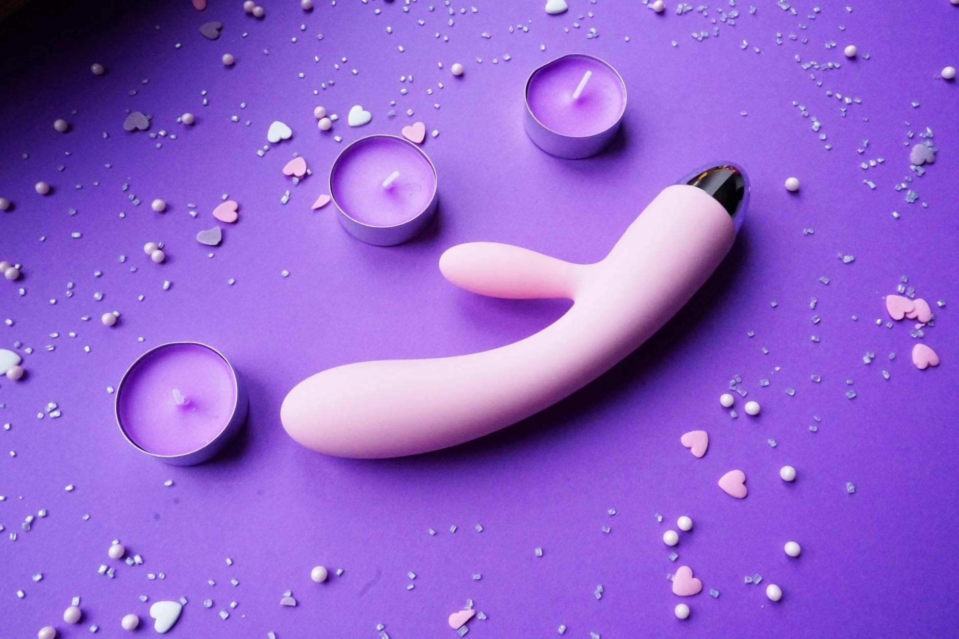 Pink vibrator on purple background with heart confetti and candles for intimate, relaxed mood