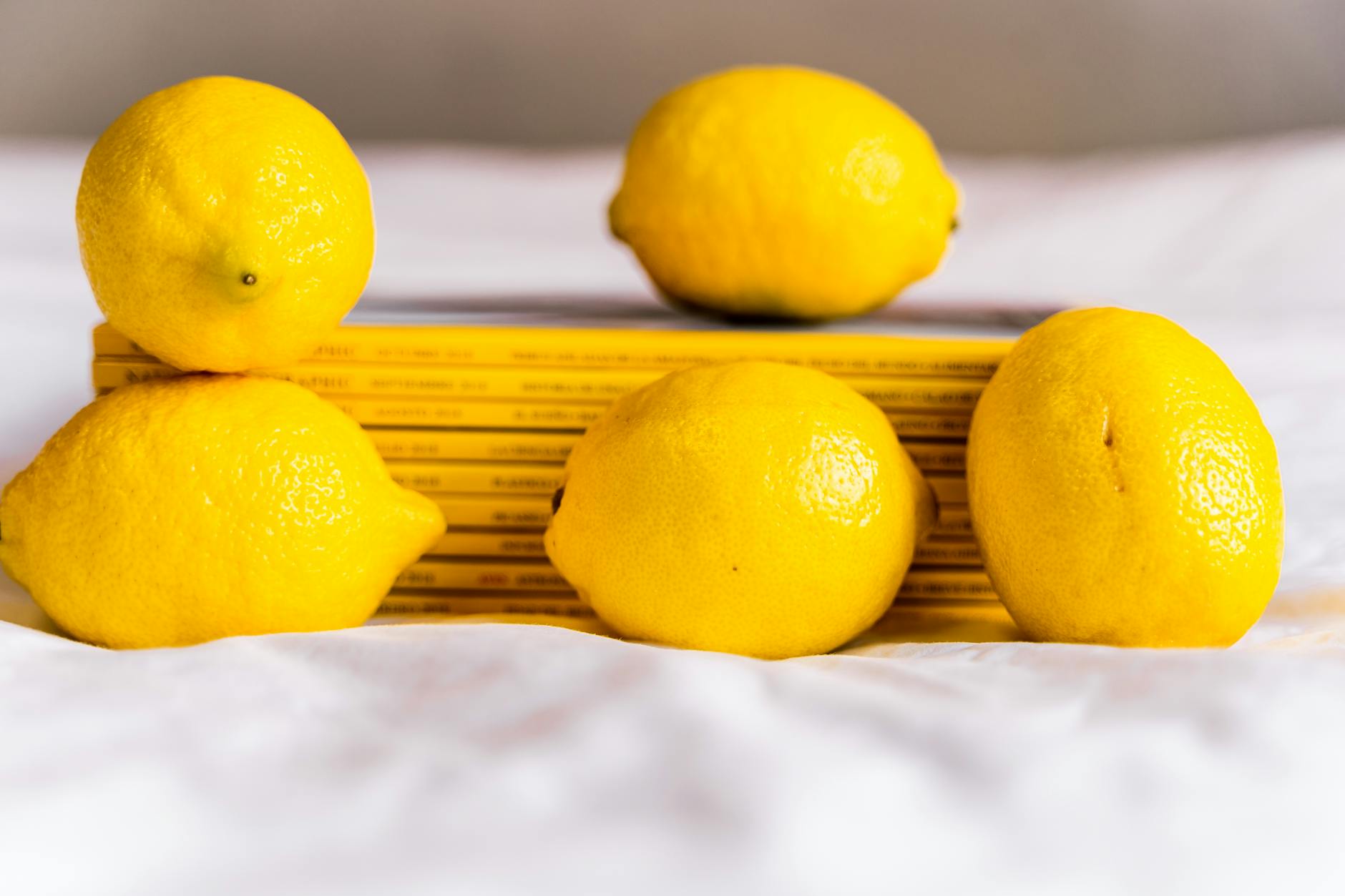 Hand holding a lemon on soft pink background, surrounded by additional lemons
